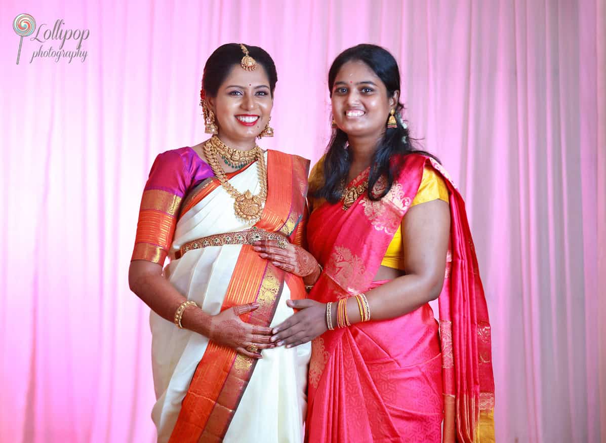 A joyous maternity portrait featuring the expectant mother in traditional attire alongside a young family member, set against a soft pink backdrop, highlighting the family’s anticipation and joy.