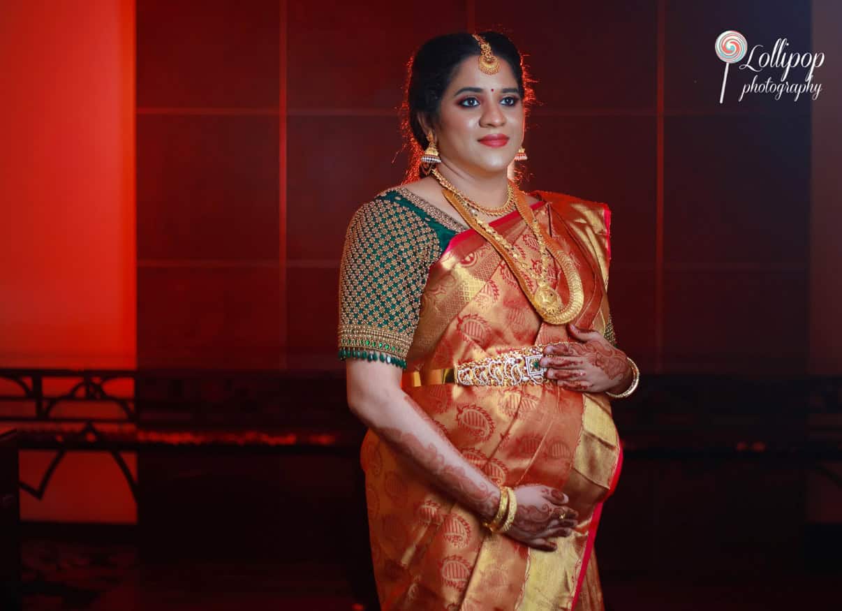 A serene portrait of a soon-to-be mother dressed in a rich green and red saree, glowing during her maternity shoot in Chennai