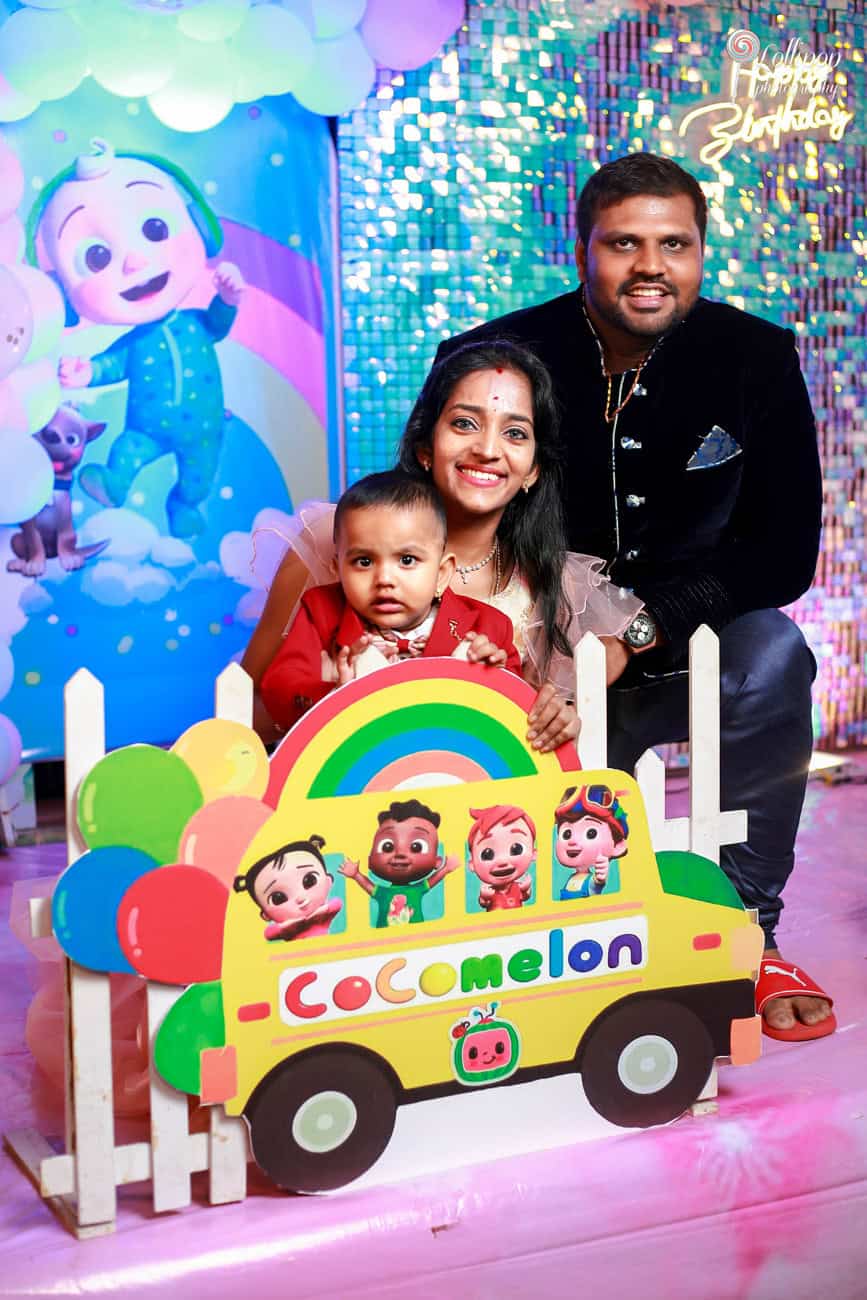 Family portrait at a cartoon-themed birthday party with vibrant colors and joyful expressions, featuring a toddler in a fun CoComelon bus, captured by Lollipop Photography in Chennai