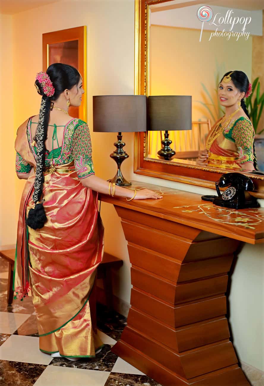 A pregnant woman in a richly embroidered traditional saree admires her reflection in a mirror, a moment captured with soft lighting and intricate interior details in Chennai.