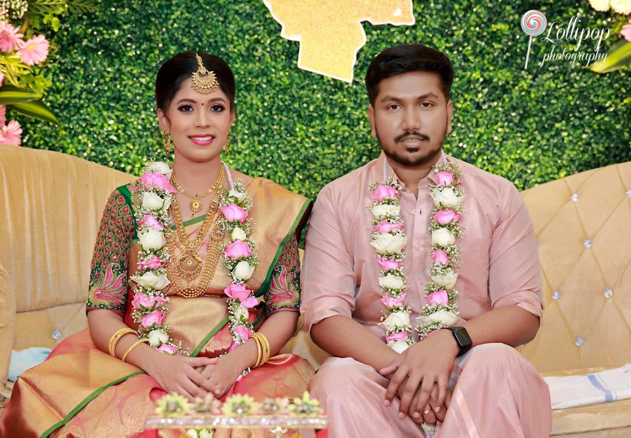 An expectant couple seated side by side, adorned with traditional garlands, surrounded by a floral and verdant setting during their baby shower celebration in Chennai.