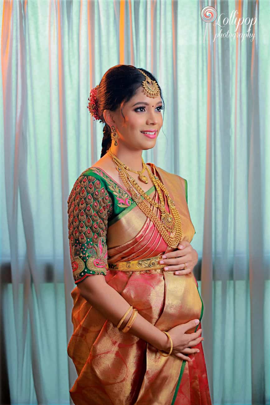 A charming portrait of a pregnant woman adorned in traditional South Indian saree and jewelry, looking pensively aside, with a gentle curtain backdrop, part of a maternity photography session in Chennai.