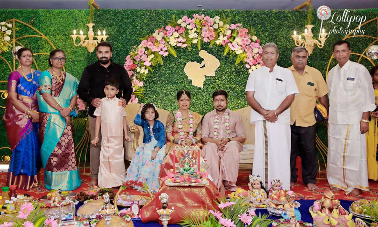 A grand family portrait during a baby shower, featuring the expectant couple centrally seated, surrounded by relatives in a decorously arranged floral setting with a vibrant green backdrop in Chennai.