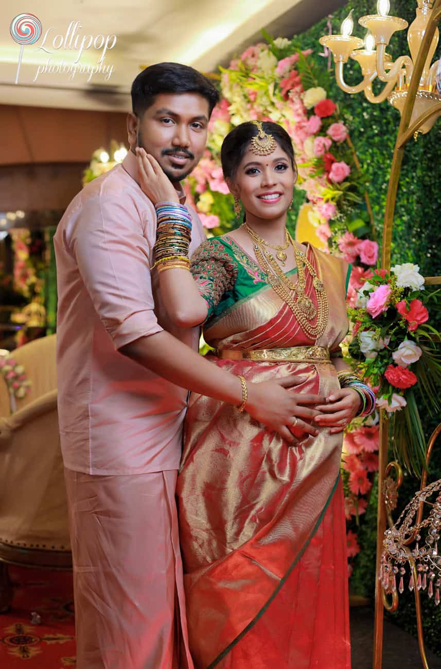 A romantic portrait of an expectant couple, the mother-to-be in a traditional saree, the father-to-be in a coordinating outfit, both radiant against a spectacular floral backdrop during their baby shower in Chennai.