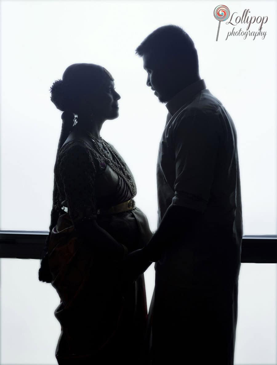 A silhouette of a pregnant couple, the woman in a traditional saree, both standing close and touching foreheads, captured against a bright light in Chennai.