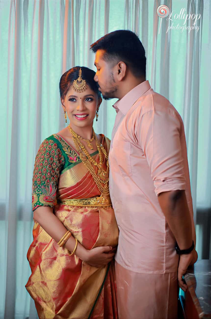 A tender moment between a pregnant woman in a traditional saree and her partner, both close and smiling, with a soft curtain backdrop in Chennai.