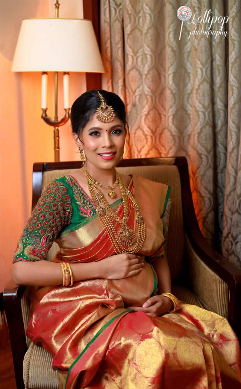 A radiant expectant mother dressed in traditional South Indian saree and elaborate gold jewelry smiles gracefully, seated in an elegant chair against a richly decorated interior in Chennai.