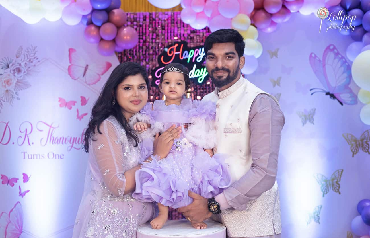 Family portrait at a first birthday party in Chennai, with parents and their child in coordinated lavender outfits, celebrating with a butterfly-themed decor, by Lollipop Photography.