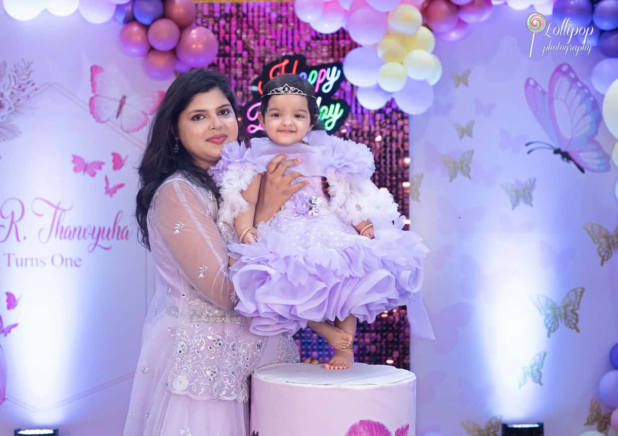 Mother and daughter sharing a tender moment at a first birthday party in Chennai, with the mother holding the birthday girl in a beautiful lavender dress, photographed by Lollipop Photography.