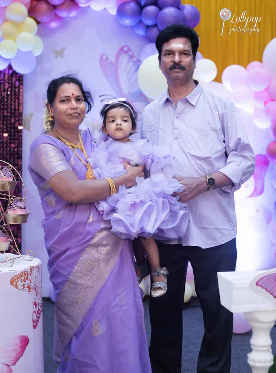 Grandparents holding their granddaughter in matching lavender attire during a first birthday celebration in Chennai, elegantly captured by Lollipop Photography.