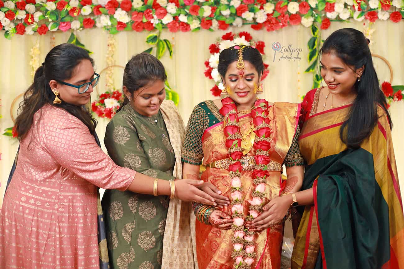 Family and friends decorating the mom-to-be with floral ornaments during her baby shower, captured by Lollipop Photography in a lush setting.