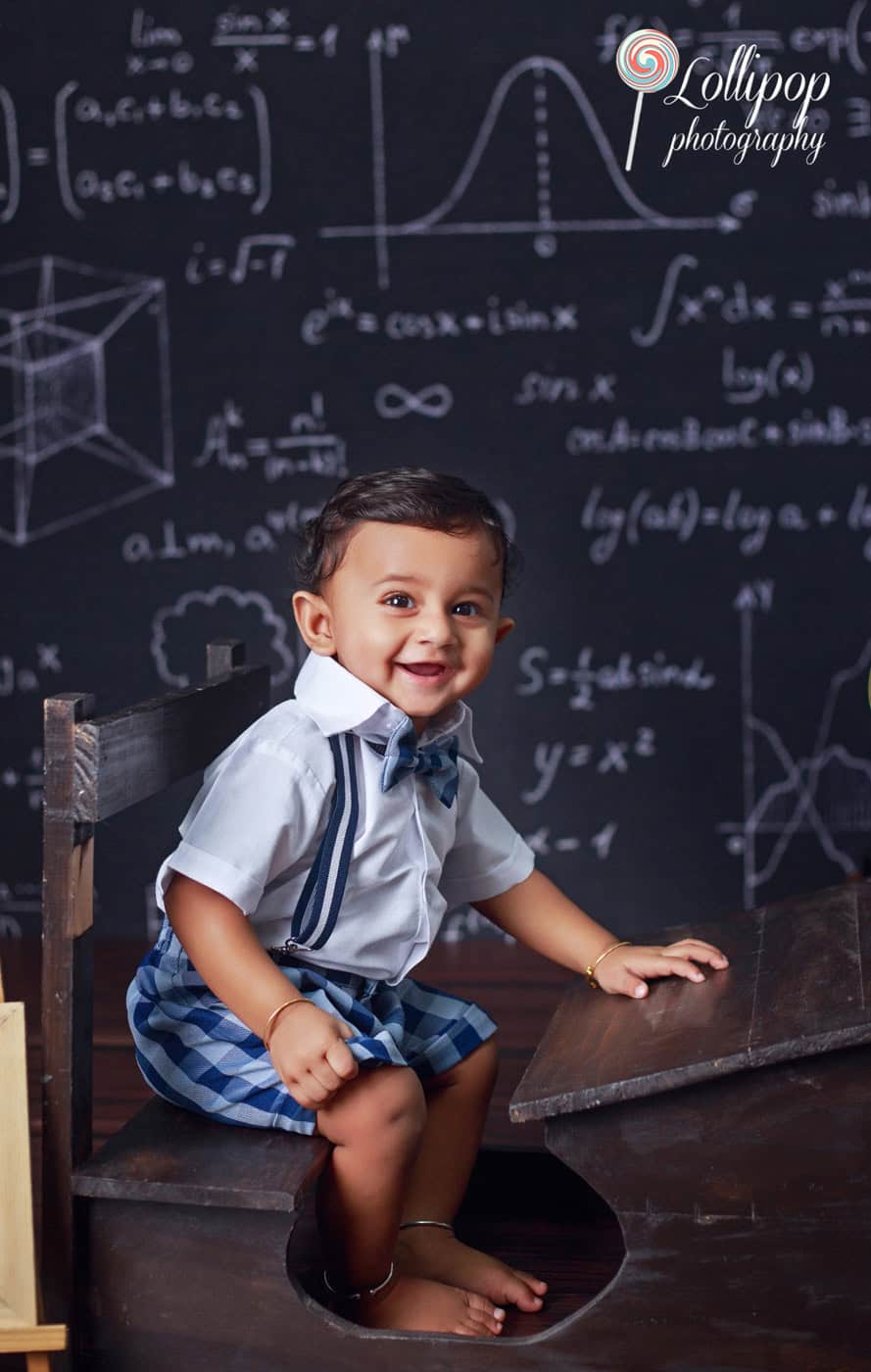 Cheerful toddler boy in school uniform at a studio photoshoot with educational chalkboard backdrop in Chennai.