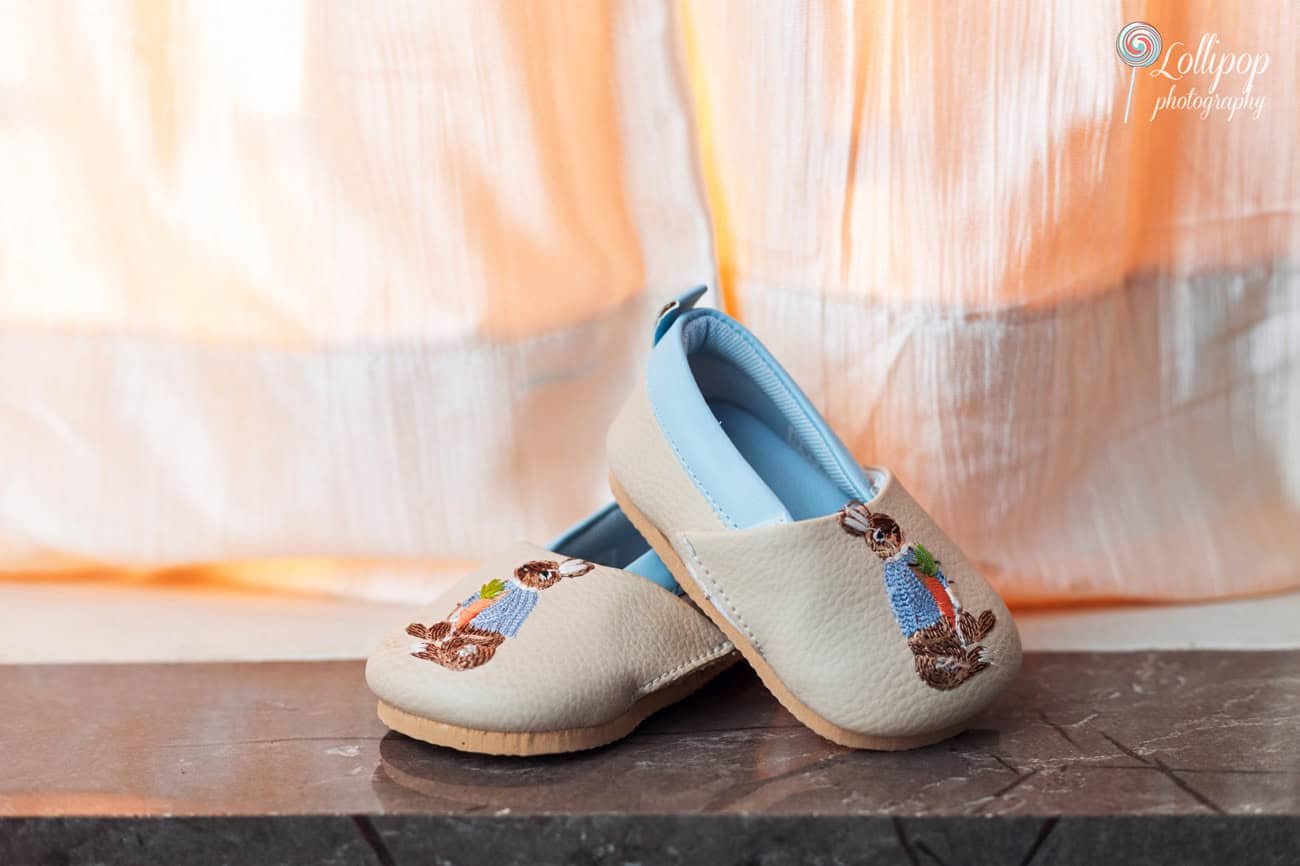 Charming pair of baby shoes embroidered with tiny birds, placed against a soft, peach-toned background, perfect for a first birthday event photoshoot by Lollipop Photography in Chennai.