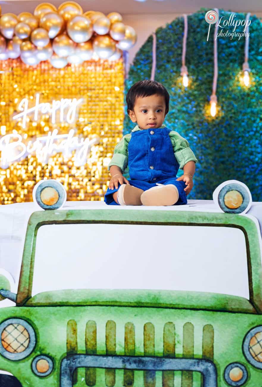 Adorable baby boy on a green toy car in front of a sparkling birthday backdrop, capturing the celebration vibes at Lollipop Photography in Chennai.