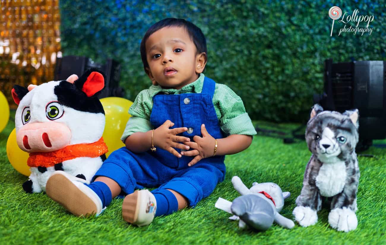 Cute scene from a first birthday with a baby surrounded by plush toys and bright yellow balloons, capturing a playful moment by Lollipop Photography in Chennai