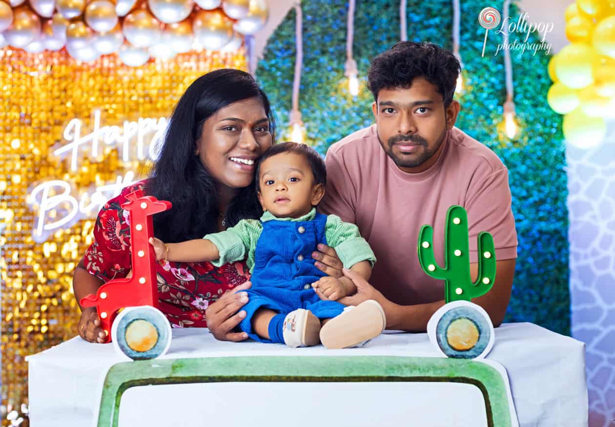 Family celebrating a child's first birthday with a colorful backdrop, featuring golden balloons and a 'Happy Birthday' sign, captured by Lollipop Photography in Chennai.