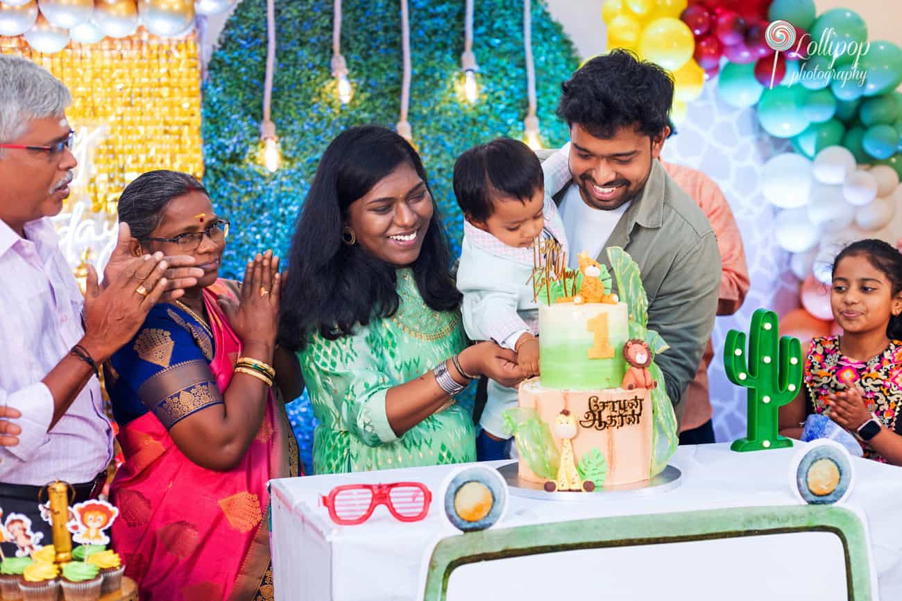 Delightful moment as family members applaud and smile while a baby reaches for the jungle-themed birthday cake, beautifully captured by Lollipop Photography in Chennai.