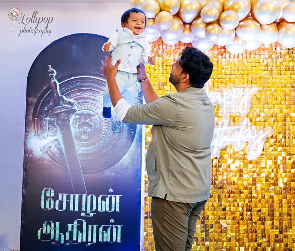 Joyful moment as a father lifts his baby boy in the air, both smiling brightly against a golden birthday backdrop, a special memory captured by Lollipop Photography in Chennai.