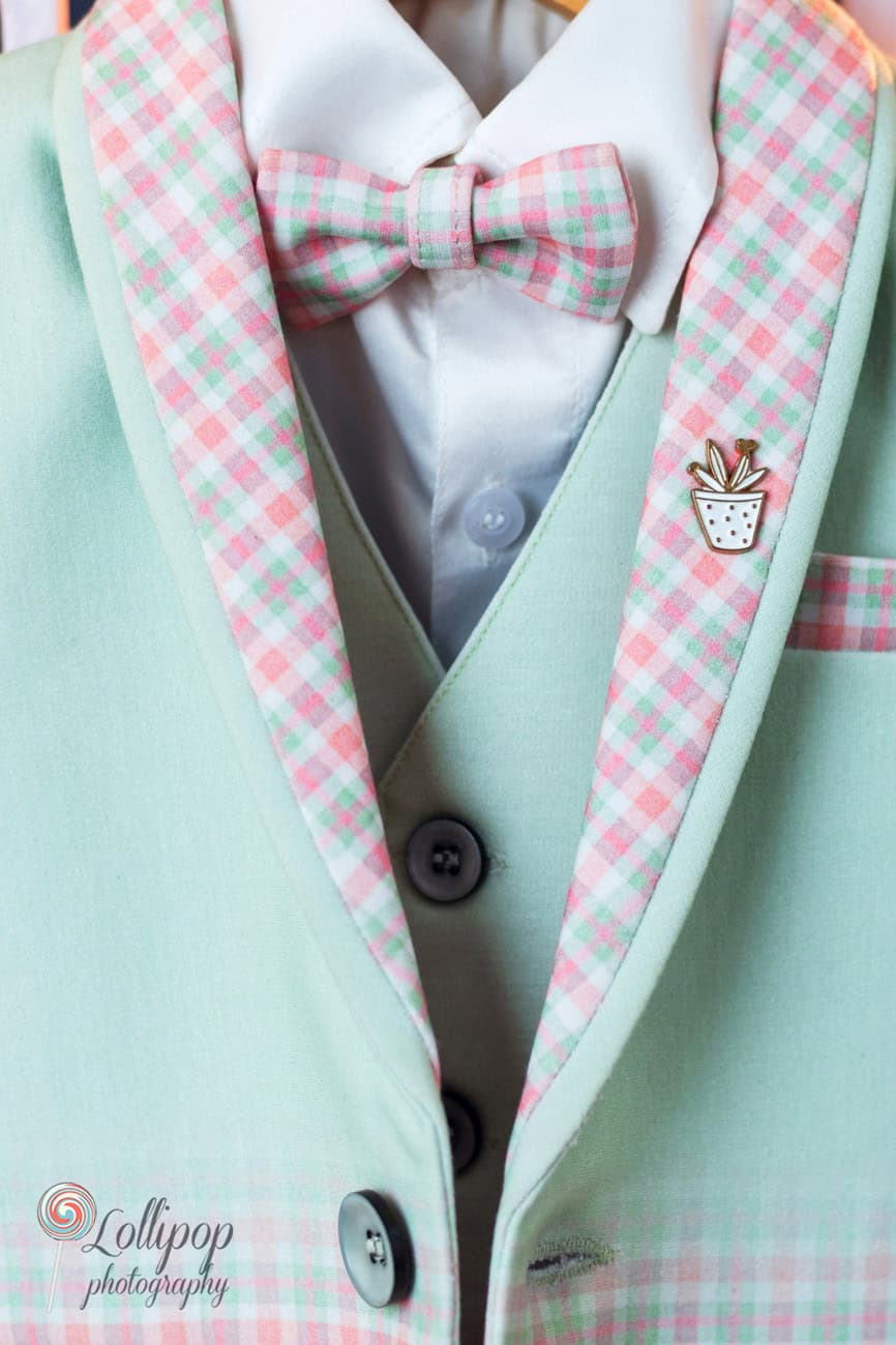 Elegant close-up of a baby's first birthday outfit featuring a mint green jacket with a plaid pink and green bow tie and a cute pineapple pin, captured by Lollipop Photography in Chennai