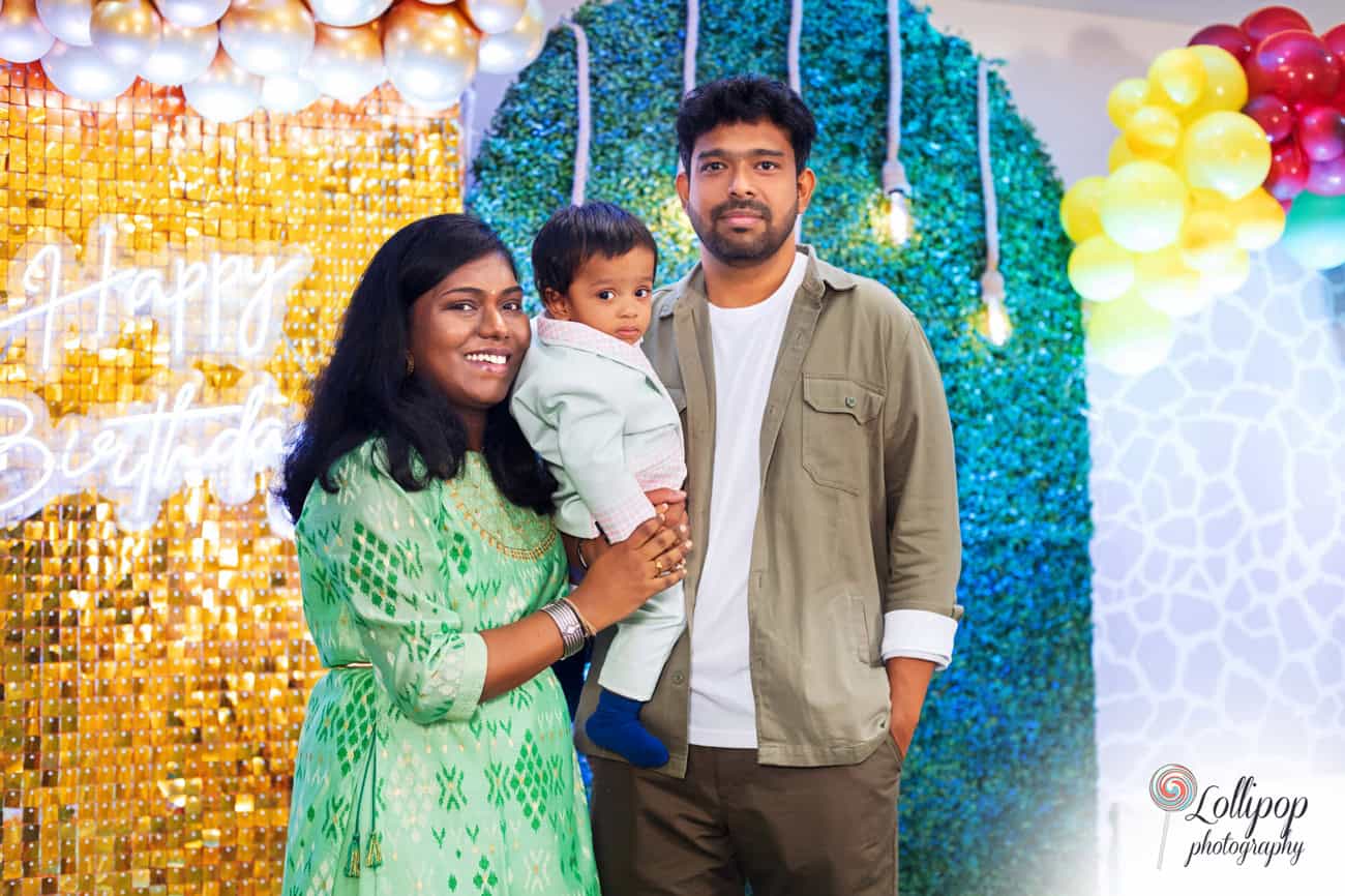 Happy family with a smiling mother, father, and their baby posing at a colorful birthday celebration, photographed by Lollipop Photography in Chennai