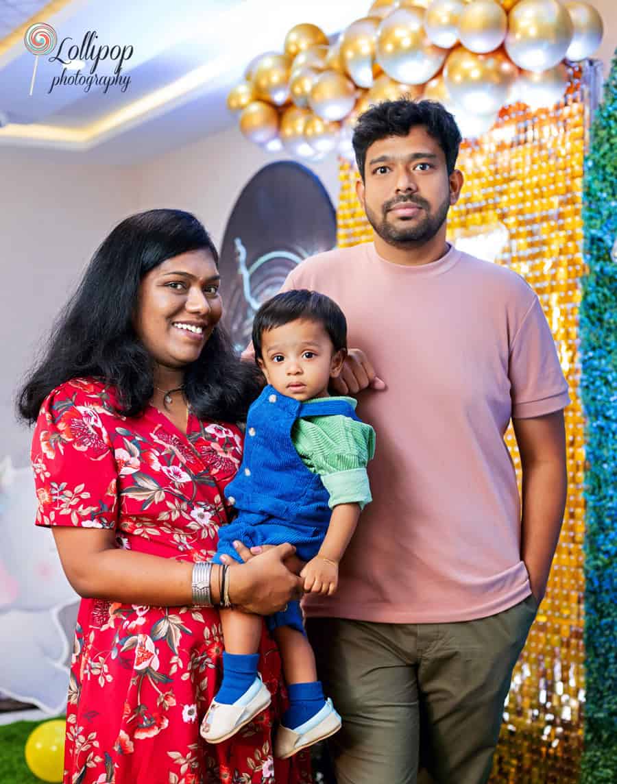 Warm family portrait with a baby, featuring a vivid and colorful birthday decoration setup, skillfully captured by Lollipop Photography in Chennai.