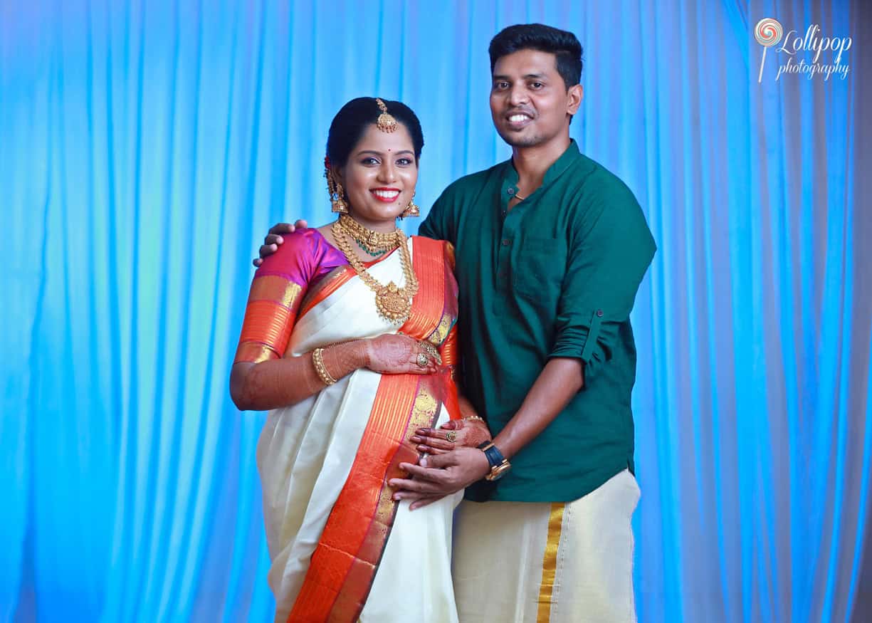 A charming couple expecting their first child, photographed in a serene blue backdrop, sharing a moment of joy in Chennai.