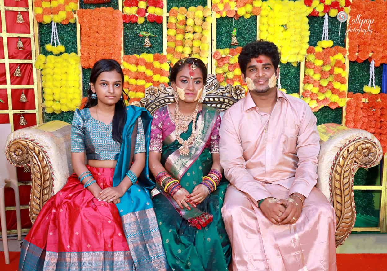 Family portrait at a baby shower, featuring a young couple seated with a child, surrounded by colorful floral decorations and cultural motifs in Coimbatore