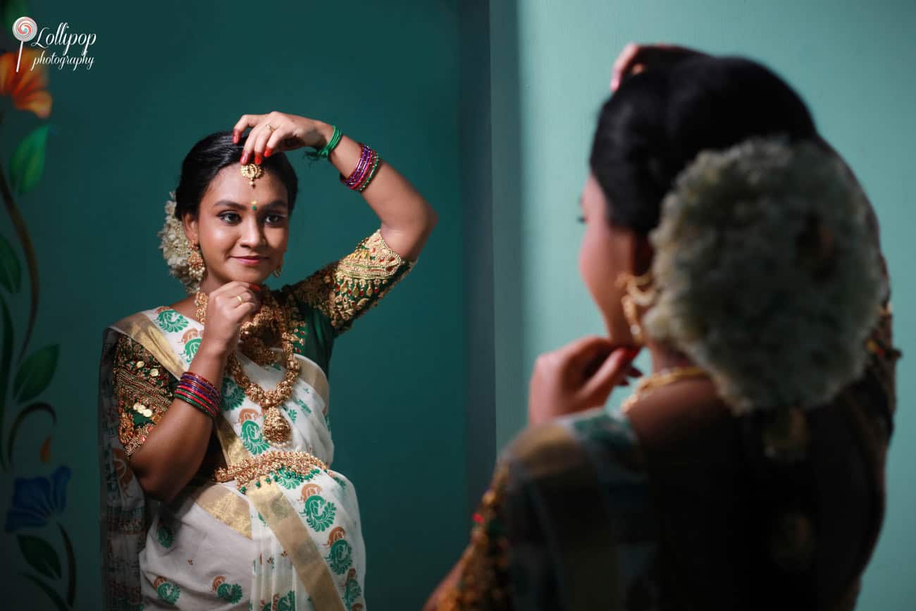 Poised expectant mother in traditional South Indian attire, adjusting her head jewelry during a maternity photoshoot in Coimbatore