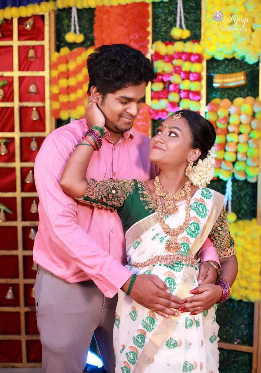 Tender moment captured between a couple during a maternity photoshoot, with the husband gently touching his wife's cheek, both smiling against a colorful floral backdrop in Coimbatore.