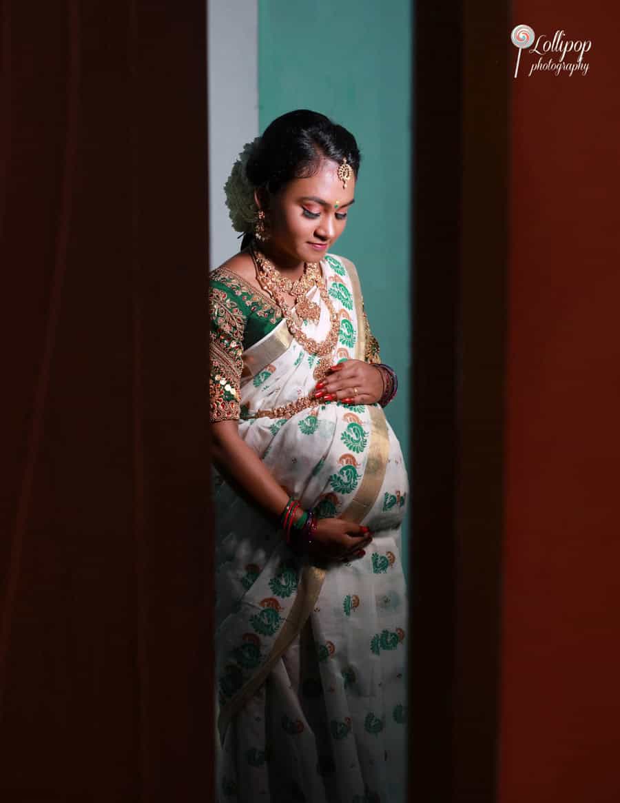 Warm-toned maternity photo of a serene expectant mother viewed through a doorway, bathed in soft light, highlighting her peaceful expression in Coimbatore.