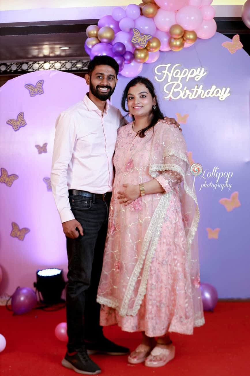 An elegant couple stands before a birthday backdrop, smiling warmly, in a photo by Lollipop Photography in Chennai.