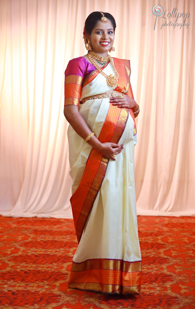 Stunning maternity photo session featuring a woman in traditional attire, her expression serene against a softly lit curtain in Chennai.