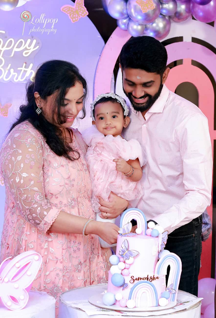 A close-knit family moment as a couple helps their daughter cut her birthday cake, surrounded by festive decorations, by Lollipop Photography in Chennai.