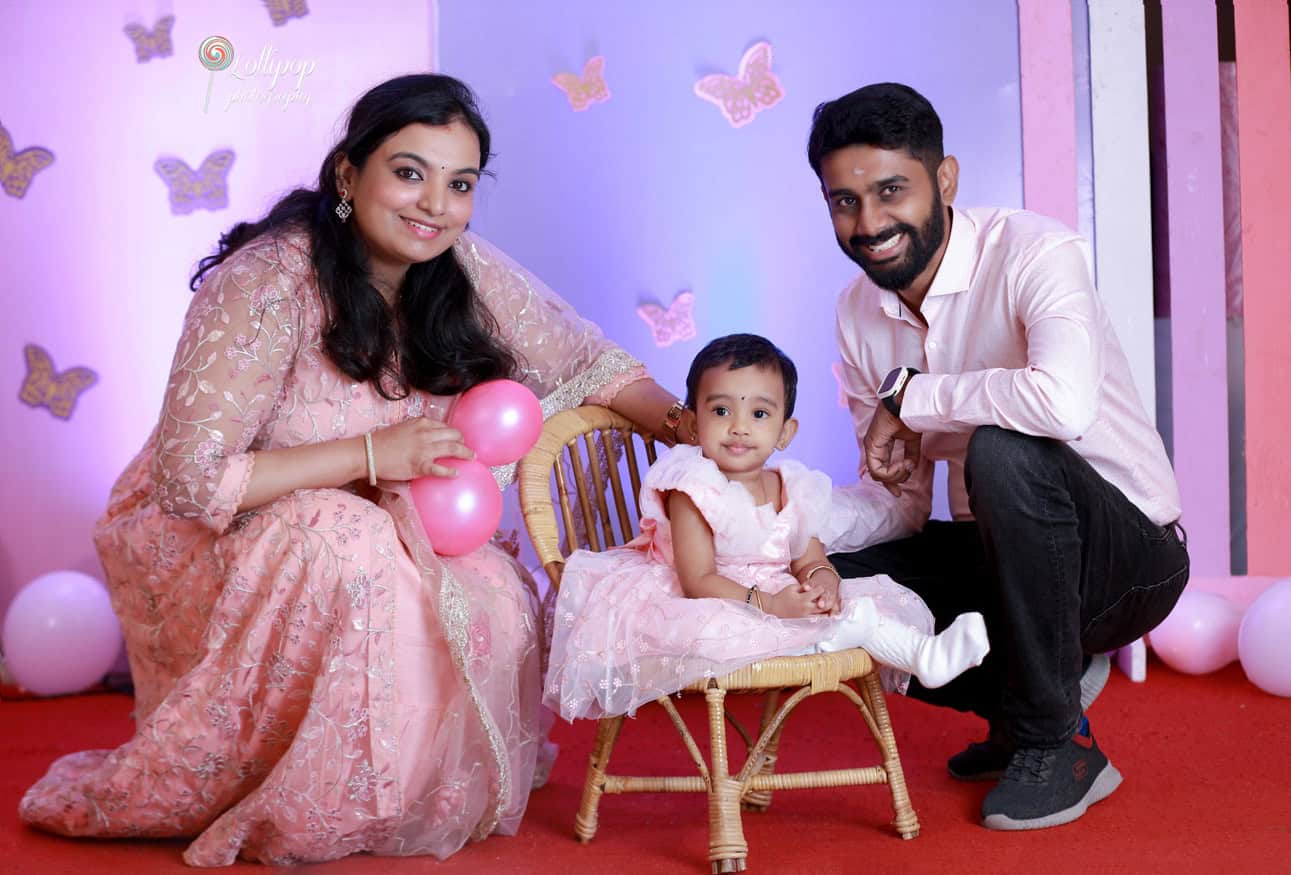 Happy family moment with a couple and their baby girl holding balloons, enjoying a playful photo session at a birthday party by Lollipop Photography in Chennai.