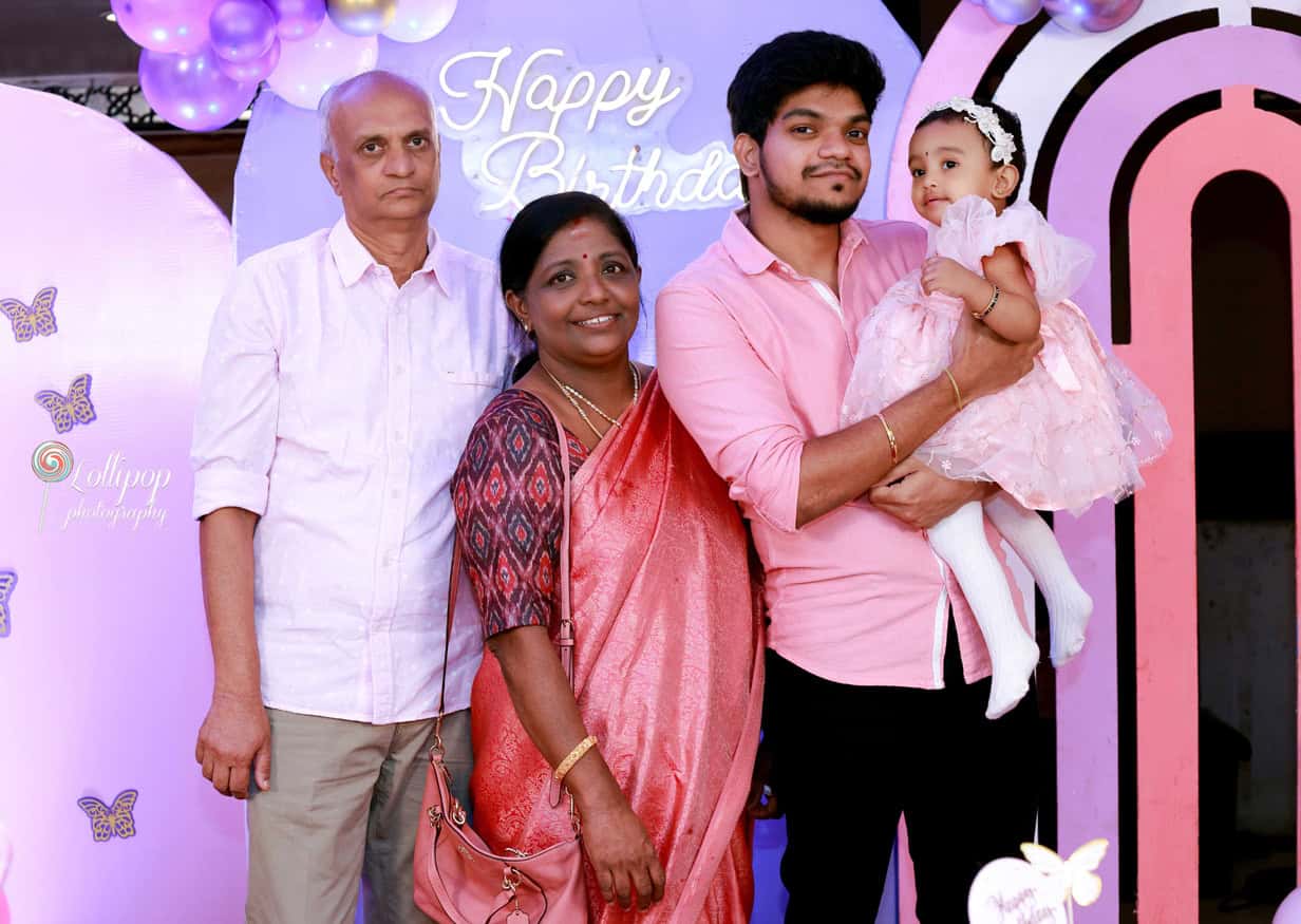 Grandparents proudly holding their granddaughter at her first birthday celebration, with a beautiful backdrop of balloons and butterfly motifs, in Chennai by Lollipop Photography.