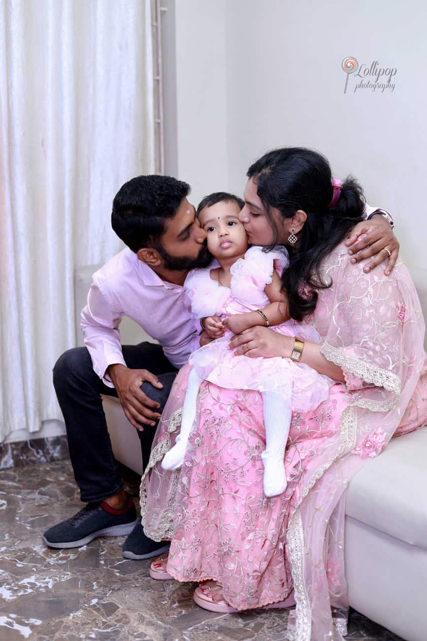 Intimate family moment showing a couple giving their baby girl kisses on the cheeks, illustrating a tender and loving family at a birthday event in Chennai by Lollipop Photography.