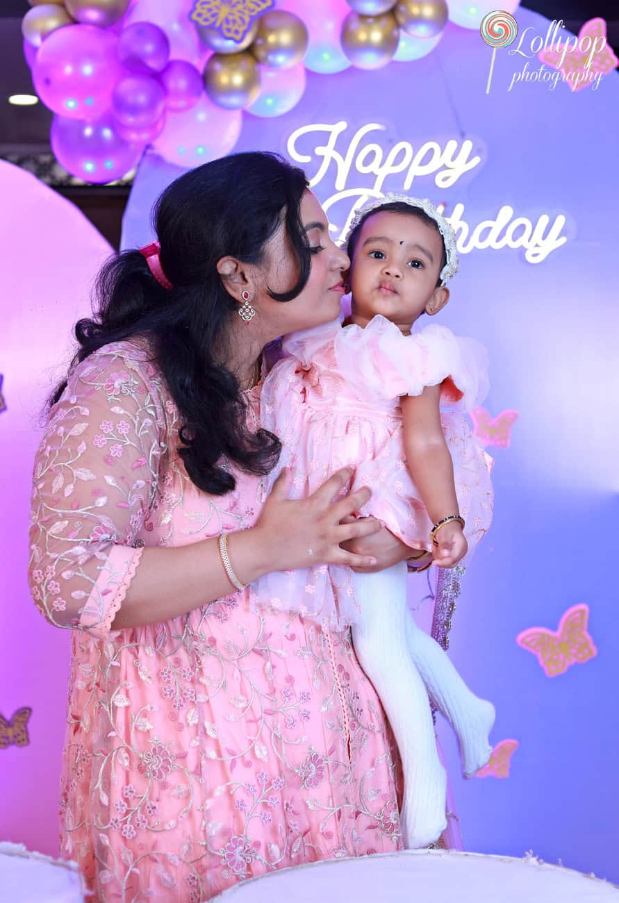 Tender moment between a mother and her daughter at a first birthday event, surrounded by balloons and butterfly motifs, photographed in Chennai by Lollipop Photography.