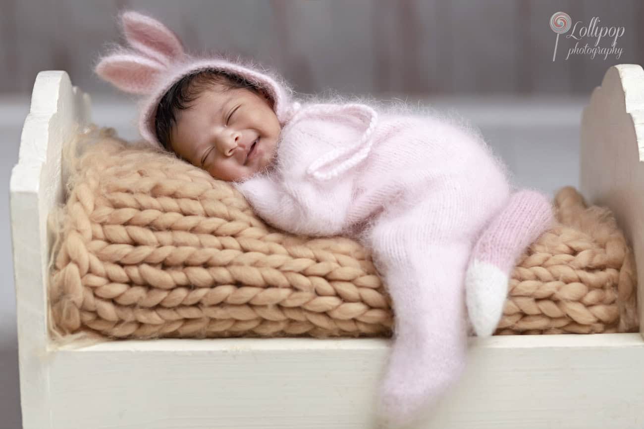 Joyful newborn in a pink bunny outfit, sleeping peacefully in a white cradle, photographed in Chennai by Lollipop Photography.