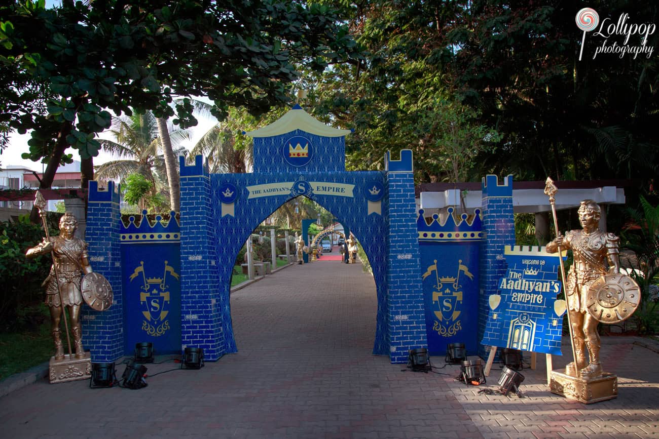 Decorative entrance arch themed as a blue medieval castle with golden statues of warriors, setting a regal tone for Aadhyans birthday celebration in Chennai.