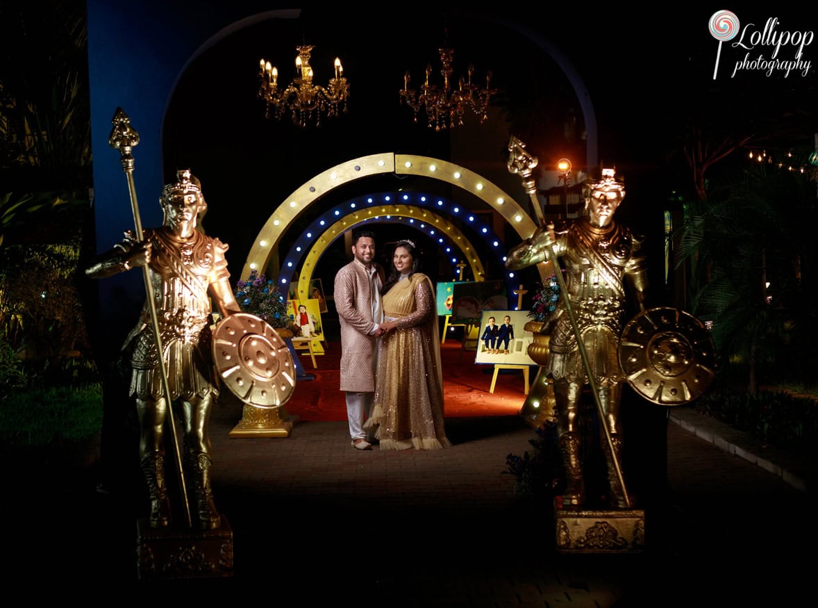 Couple posing at a birthday celebration under a lit archway flanked by golden warrior statues, creating a majestic entrance in Chennai.