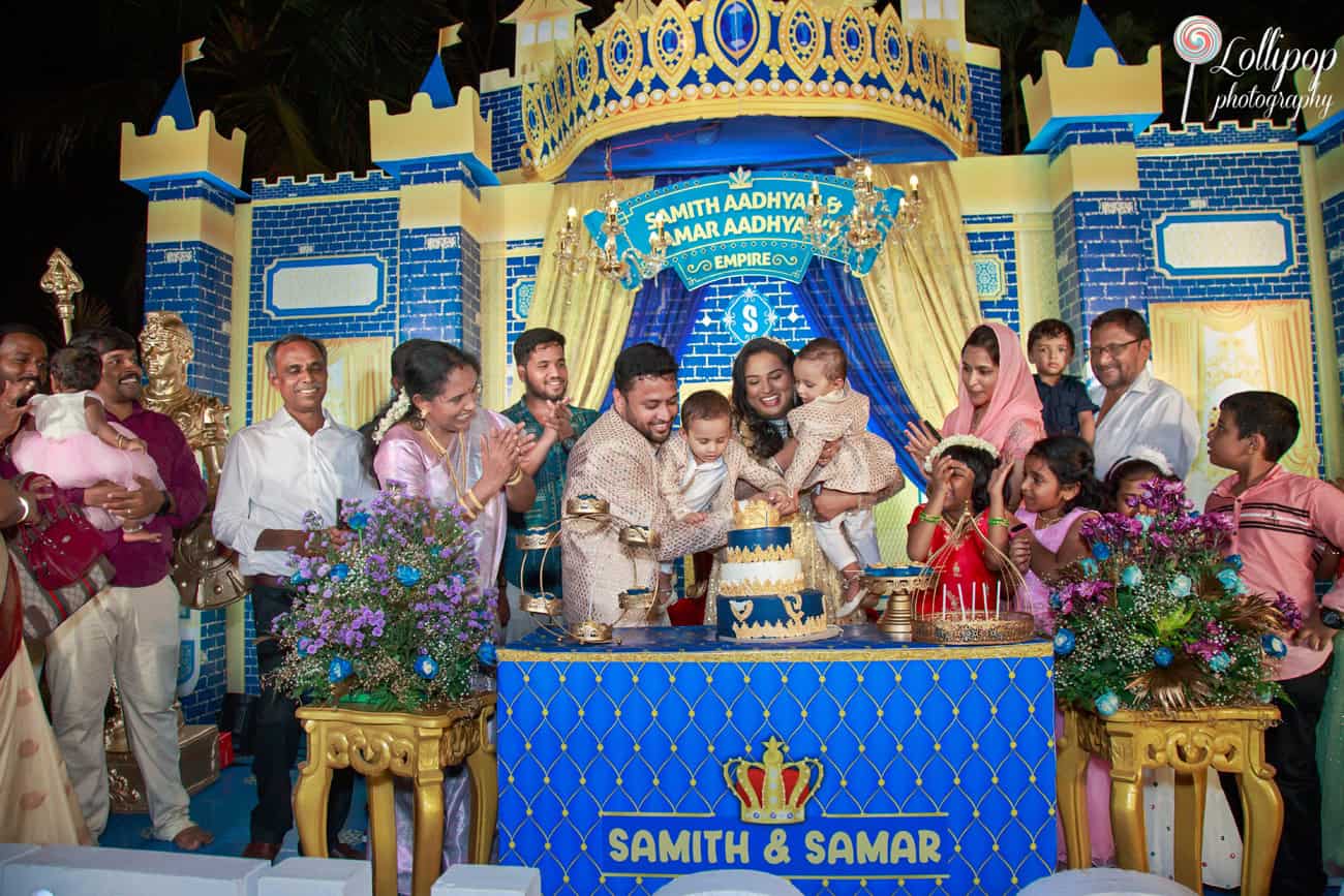 Joyous family celebration at a birthday party in Chennai with parents and children cutting a large blue and gold cake surrounded by family and friends cheering.