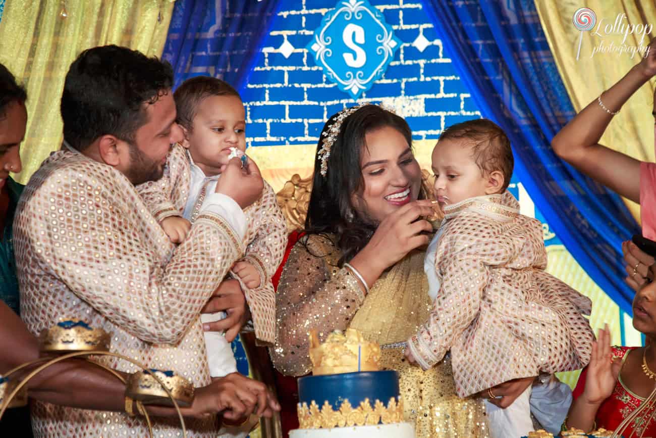 Heartwarming scene of parents feeding birthday cake to their twin toddlers during a festive celebration, with family and friends in the background in Chennai.