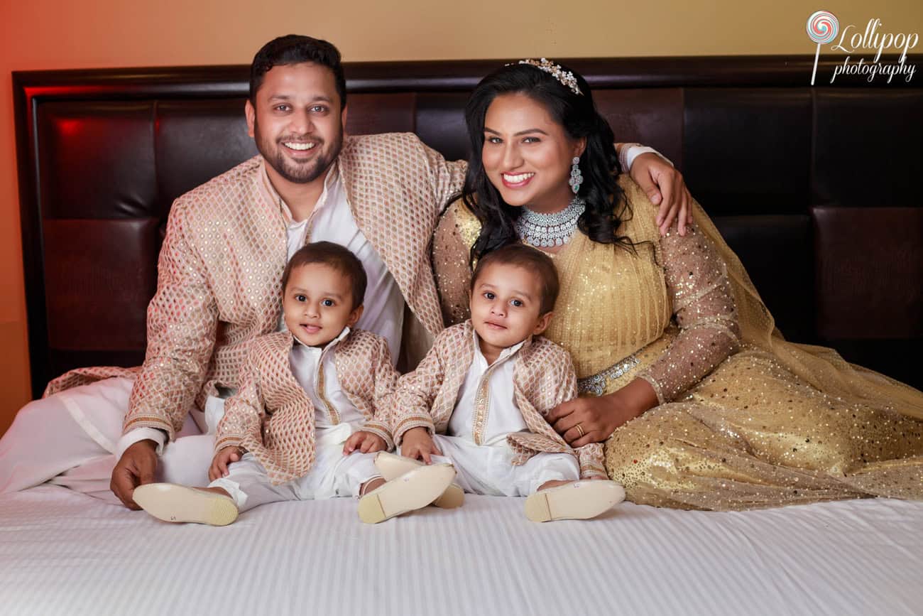 Warm family photo featuring parents and twin toddlers lying comfortably on a bed, smiling at the camera, dressed in elegant traditional outfits in Chennai.