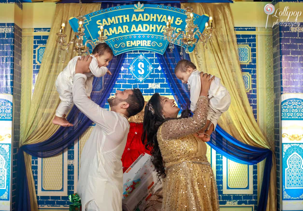 Playful and loving family interaction with parents lifting their twins in the air, celebrating their birthday near a regal blue throne in Chennai