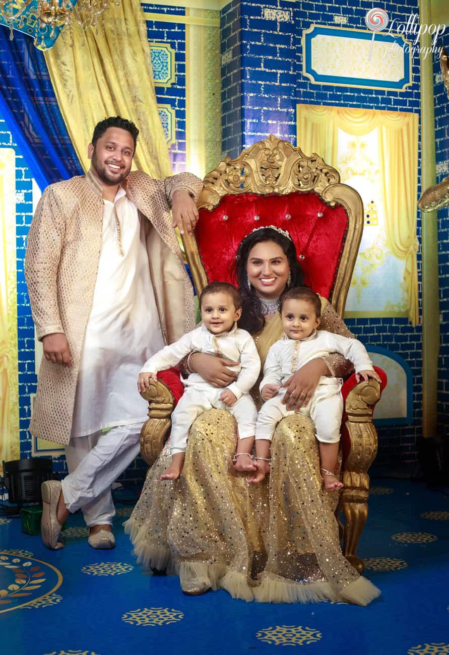 Elegant family portrait on a red royal throne at a birthday party, featuring parents seated with their twins in matching traditional attire in Chennai.