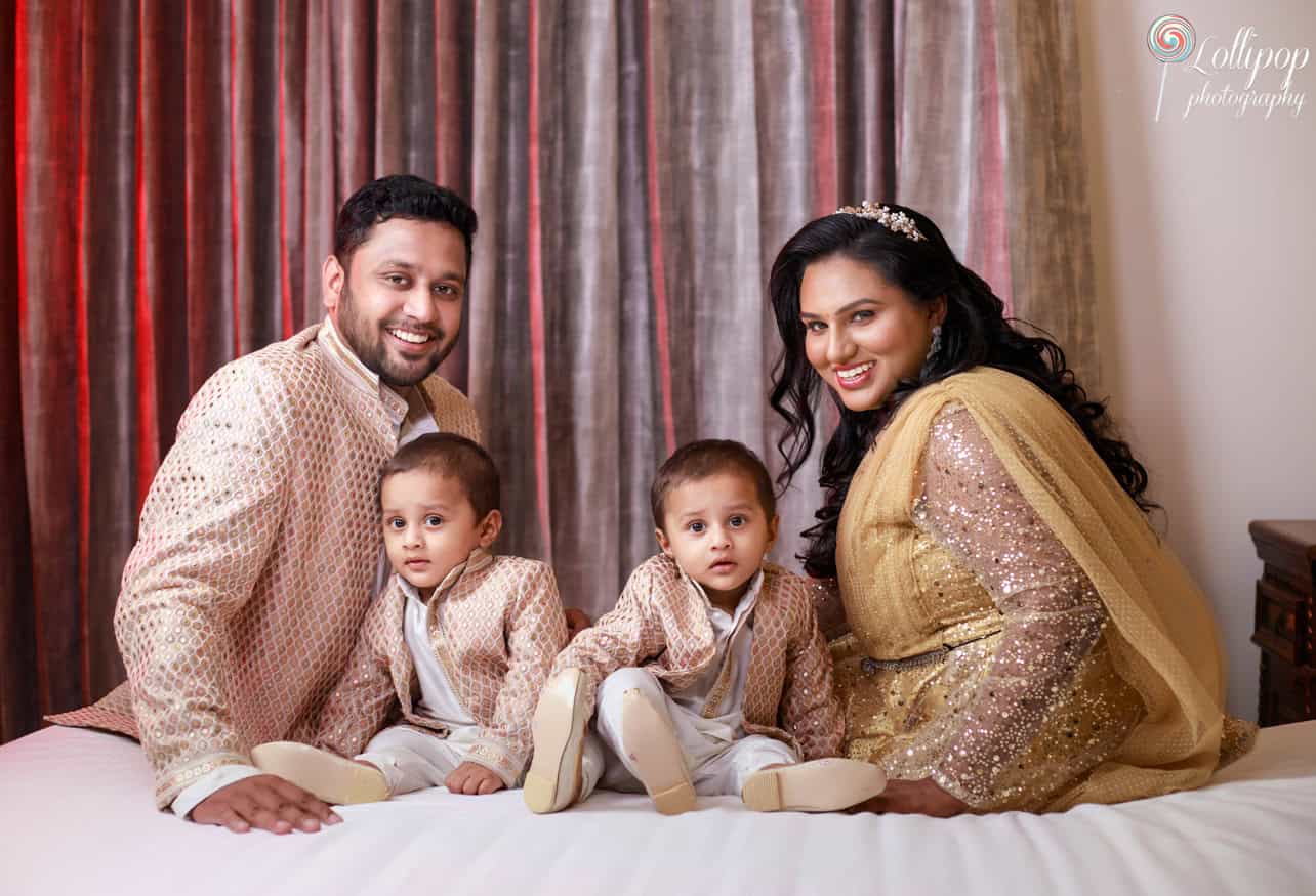 Relaxed family portrait on a bed with parents and their twin boys in coordinating outfits, capturing a serene moment at their home in Chennai.