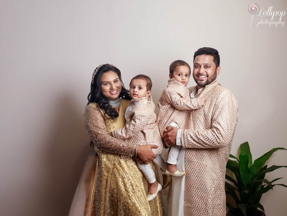 A radiant family portrait featuring a couple in traditional attire holding their twin boys during a birthday celebration in Chennai.