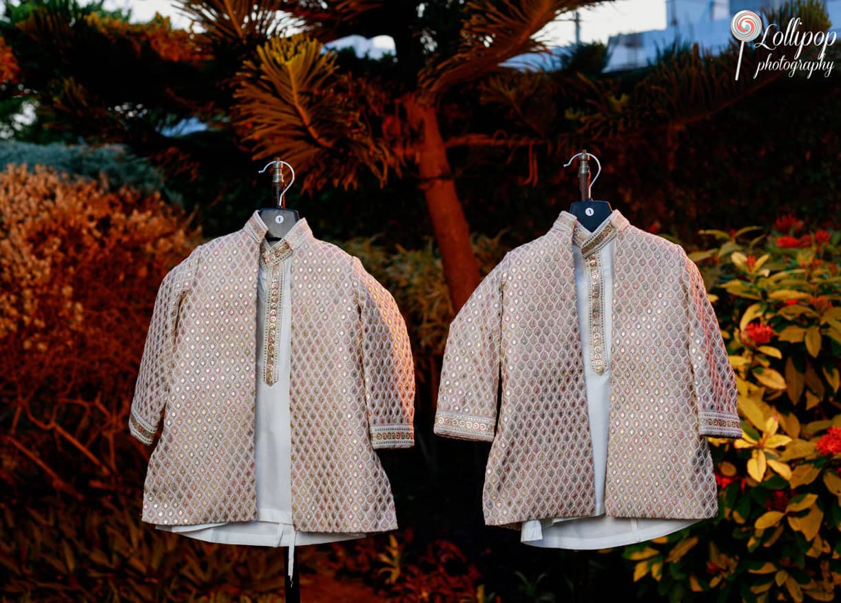 Two traditional Indian boys' outfits with intricate designs, displayed outdoors against a backdrop of lush greenery, ready for a birthday celebration in Chennai