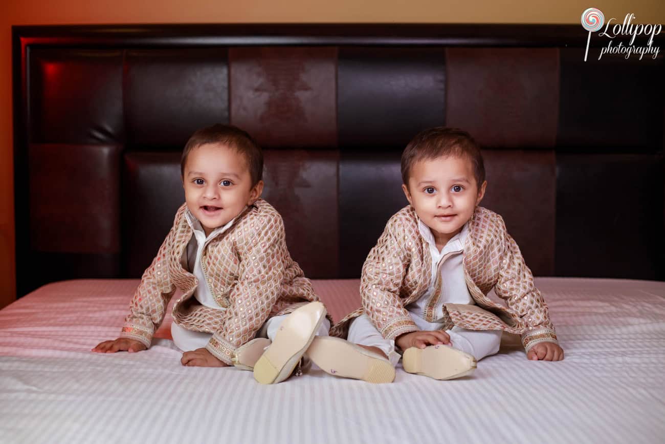 Adorable twin toddlers sitting on a bed, dressed in matching traditional attire, with a look of curiosity, captured in Chennai