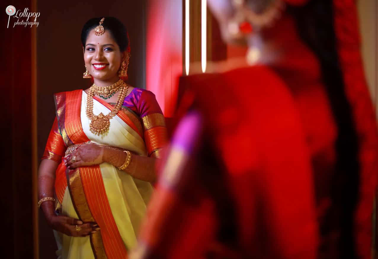 Expectant mother in a reflective pose, showcasing her ornate jewelry and henna-decorated hands, at her baby shower event in Chennai, by Lollipop Photography.